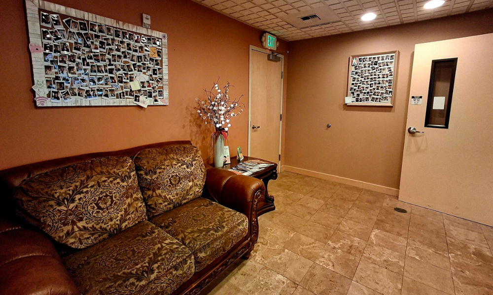 Dental office waiting room with patterned sofa, patient photo boards, and decorative floral arrangement on side table