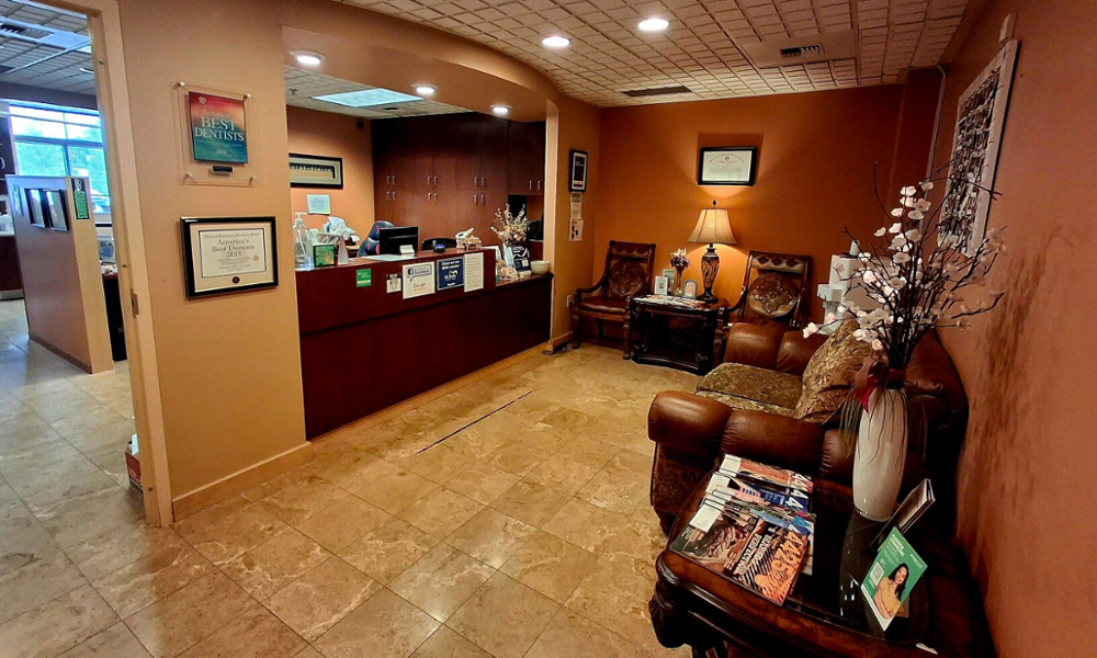 Warm dental office reception area with wood front desk, leather seating, awards, and floral decor